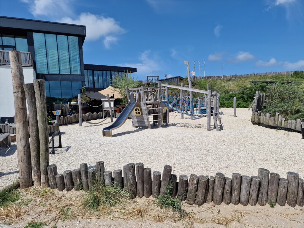 Speelplek met natuurlijke ondergrond, houten elementen en gevarieerde speelaanleidingen voor kinderen van verschillende leeftijden